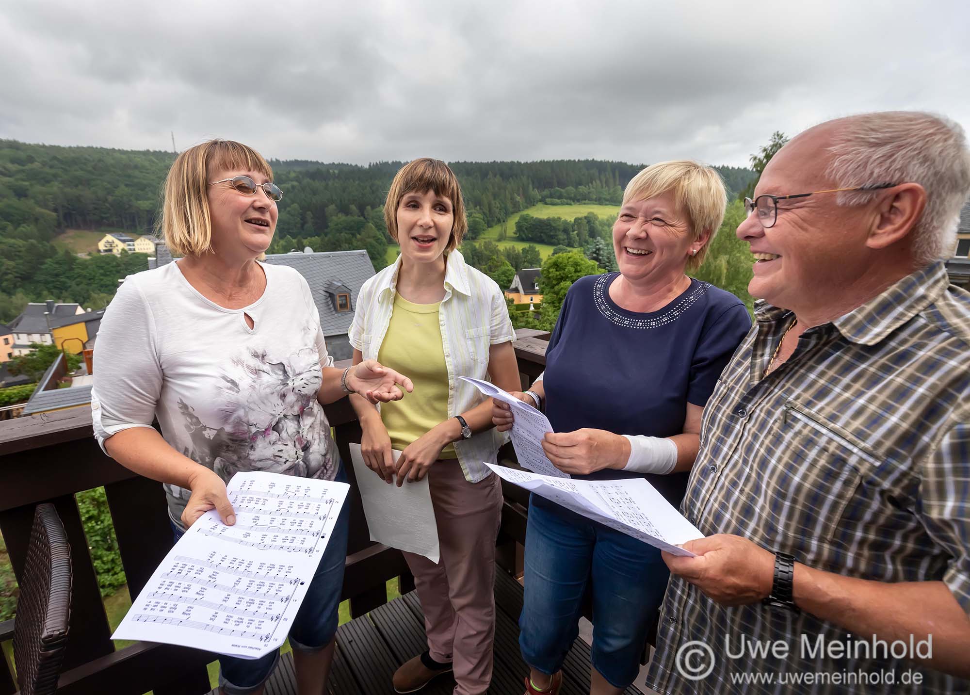 Wir, Heike, Birgit, Gabi und Winfried, stehen mit Notenblättern in der Hand auf dem Balkon und haben Spaß am Singen